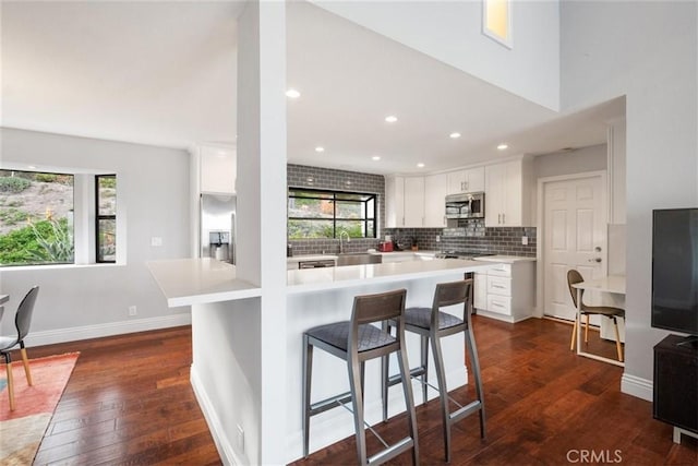 kitchen with kitchen peninsula, stainless steel appliances, white cabinets, a kitchen breakfast bar, and decorative backsplash