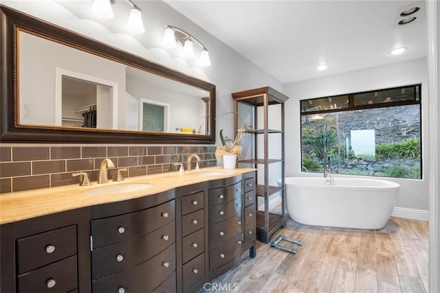 bathroom featuring a washtub, vanity, backsplash, and hardwood / wood-style floors