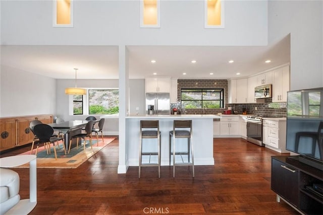 kitchen with appliances with stainless steel finishes, dark wood-type flooring, pendant lighting, backsplash, and white cabinetry