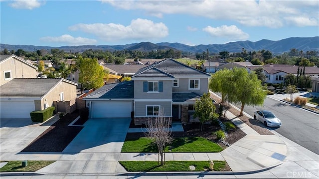 view of front of property featuring a garage, concrete driveway, stone siding, a residential view, and a mountain view