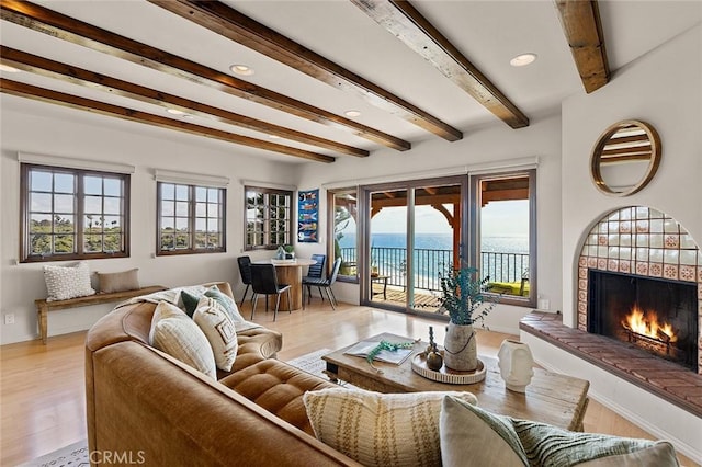 living room with a water view, a lit fireplace, light wood-style flooring, and beam ceiling