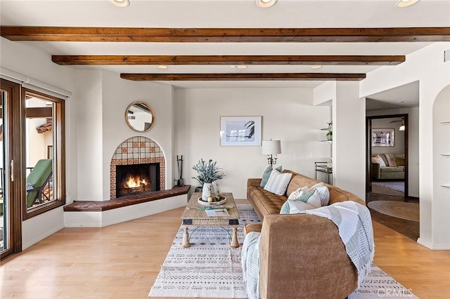 living room featuring a lit fireplace, baseboards, light wood-style flooring, and beamed ceiling