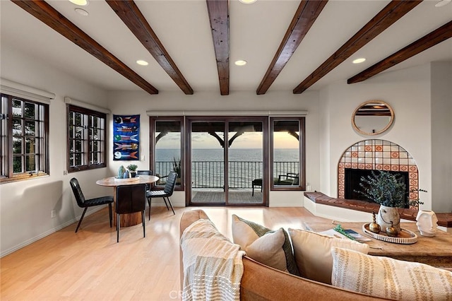 living room featuring recessed lighting, a water view, light wood-style floors, a tile fireplace, and baseboards