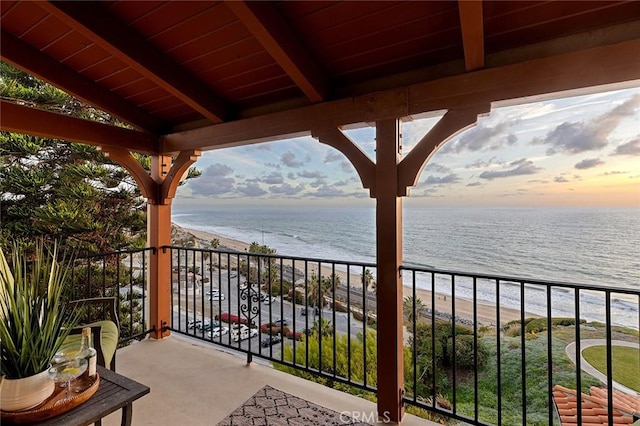 balcony at dusk with a water view and a view of the beach