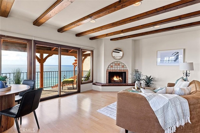 living room with a warm lit fireplace, light wood finished floors, a water view, and beam ceiling