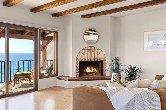 living room featuring a water view, a fireplace, beamed ceiling, and light wood finished floors