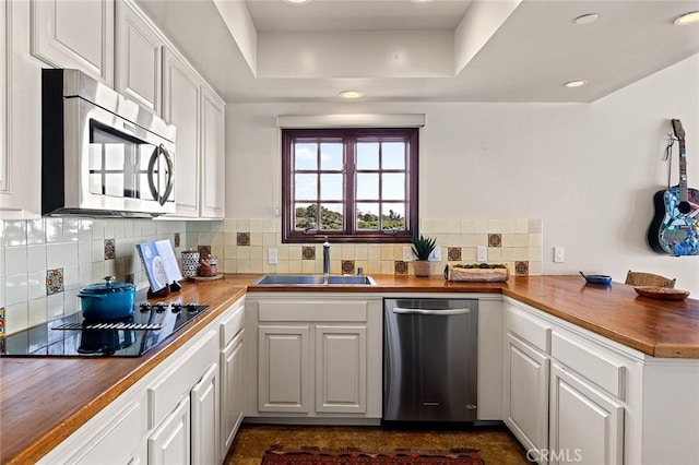 kitchen featuring stainless steel appliances, a sink, wood counters, white cabinets, and a tray ceiling