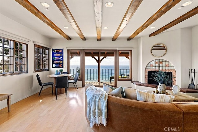 living room with a fireplace with raised hearth, a water view, baseboards, light wood finished floors, and beamed ceiling