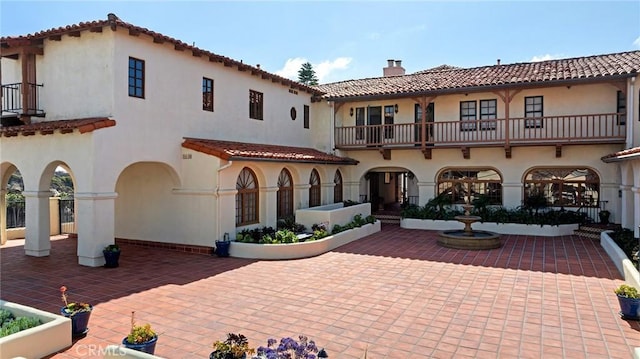 view of front of home with a tile roof, a chimney, stucco siding, a patio area, and a balcony