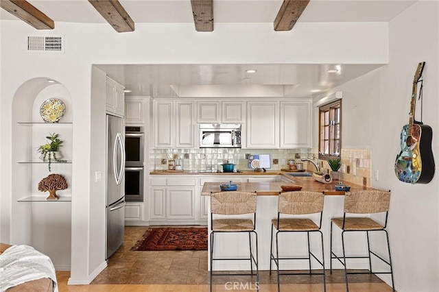 kitchen with stainless steel appliances, a peninsula, a sink, visible vents, and white cabinetry