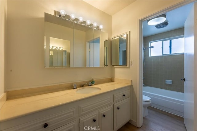 full bathroom with vanity, tiled shower / bath, hardwood / wood-style flooring, and toilet