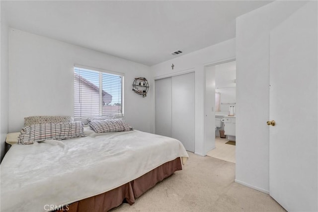 bedroom with connected bathroom, light carpet, and a closet