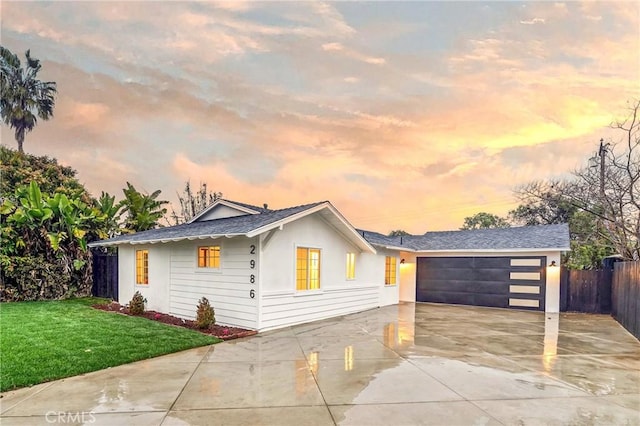 view of front of house with a shingled roof, concrete driveway, a front lawn, and fence