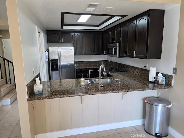 kitchen with dark stone countertops, sink, stainless steel appliances, and kitchen peninsula