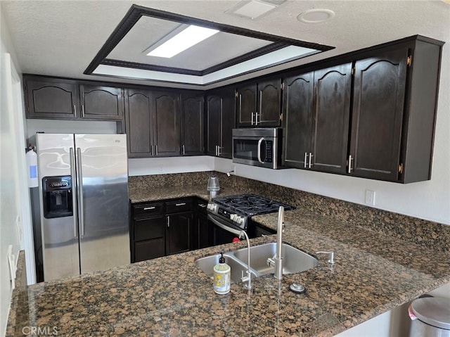 kitchen with dark brown cabinetry, stainless steel appliances, a raised ceiling, and dark stone counters