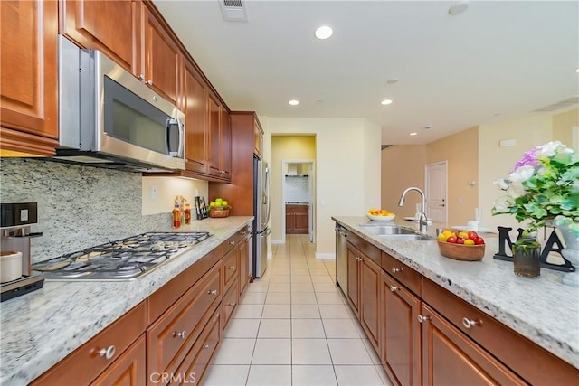 kitchen with appliances with stainless steel finishes, sink, backsplash, light tile patterned floors, and light stone counters