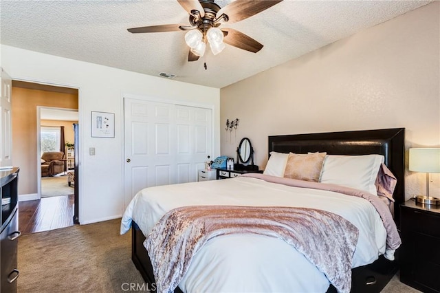 bedroom with a closet, visible vents, dark carpet, a textured ceiling, and baseboards