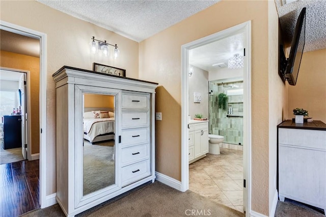 bathroom with a textured ceiling, connected bathroom, vanity, baseboards, and a shower stall