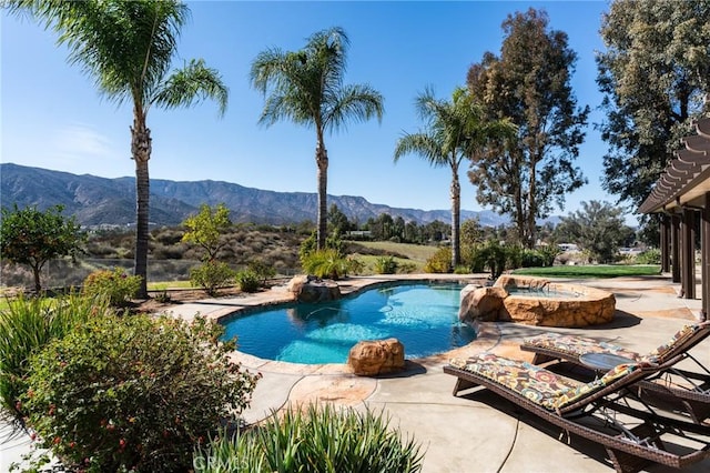 pool with a patio area, a mountain view, and an in ground hot tub