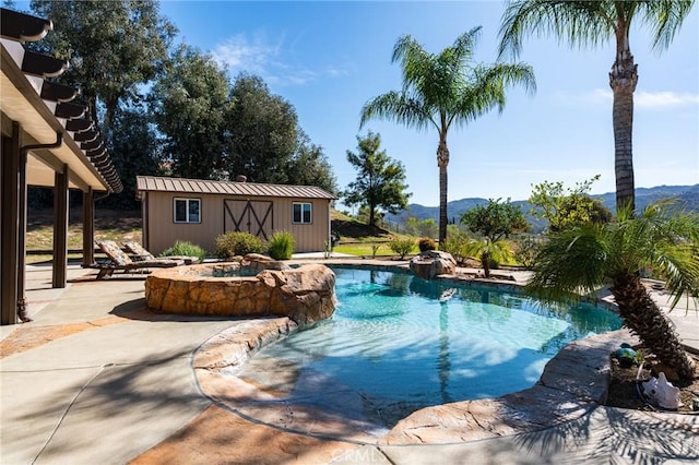 outdoor pool with an in ground hot tub, a mountain view, a patio, and an outbuilding