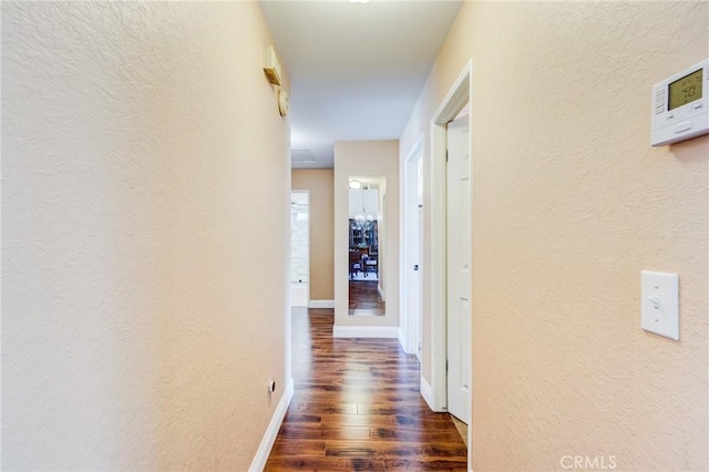 hall featuring baseboards, dark wood-type flooring, and a textured wall