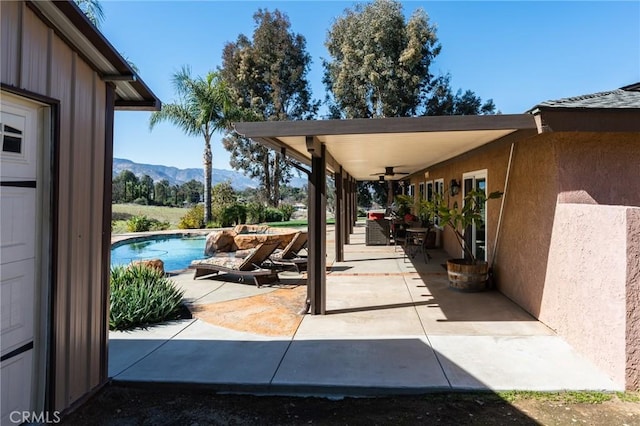 view of patio / terrace with a ceiling fan, a mountain view, and an outdoor pool