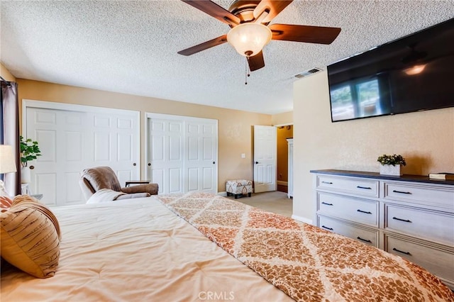 bedroom featuring visible vents, ceiling fan, carpet, a textured ceiling, and two closets