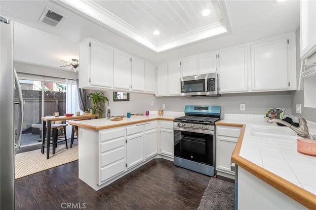 kitchen featuring appliances with stainless steel finishes, tile counters, a tray ceiling, kitchen peninsula, and white cabinets