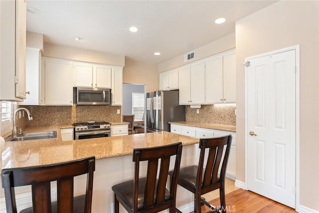 kitchen with appliances with stainless steel finishes, sink, white cabinetry, and a breakfast bar