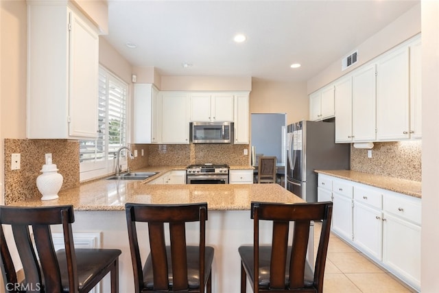 kitchen featuring appliances with stainless steel finishes, sink, white cabinetry, a kitchen breakfast bar, and kitchen peninsula