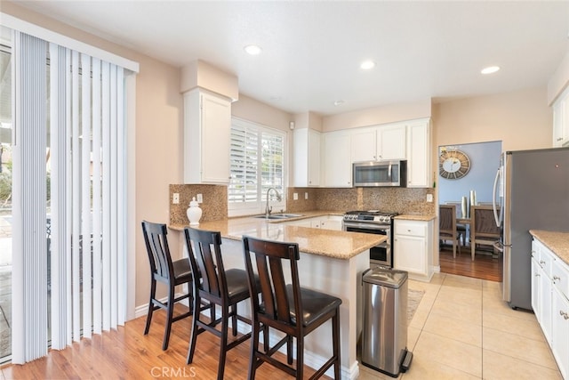 kitchen with sink, white cabinetry, a kitchen breakfast bar, stainless steel appliances, and kitchen peninsula