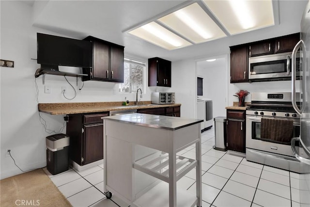 kitchen featuring washing machine and clothes dryer, dark brown cabinetry, sink, light tile patterned floors, and stainless steel appliances