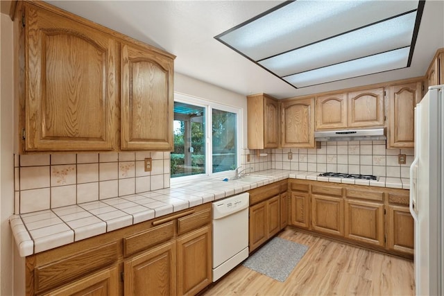 kitchen with sink, decorative backsplash, tile counters, white appliances, and light hardwood / wood-style flooring