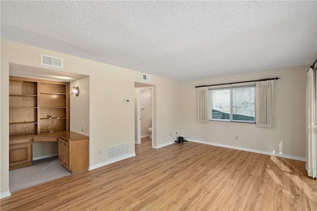 unfurnished living room with built in desk, a textured ceiling, and light wood-type flooring