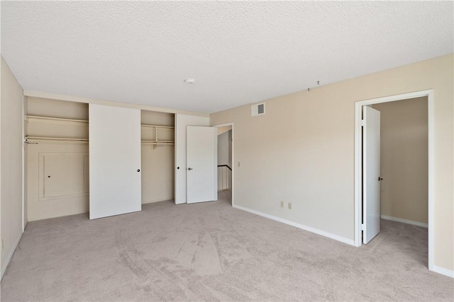 unfurnished bedroom featuring light carpet, two closets, and a textured ceiling