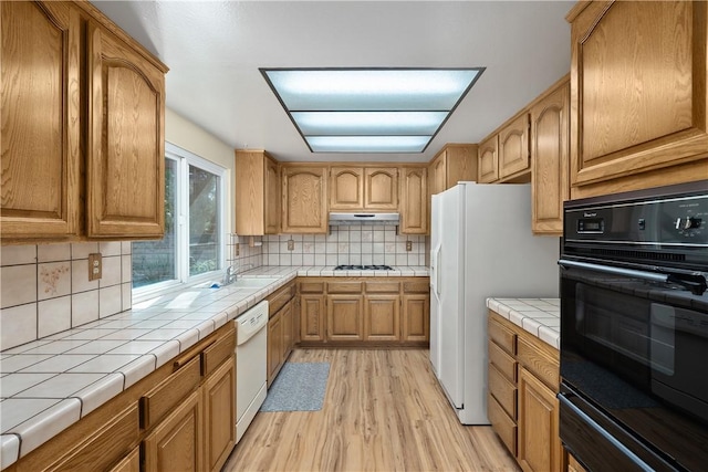 kitchen featuring sink, backsplash, tile counters, white appliances, and light hardwood / wood-style flooring