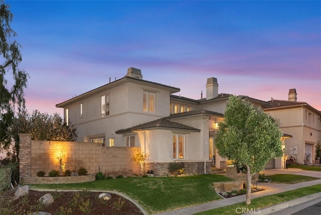 back of property at dusk featuring stone siding, stucco siding, and fence