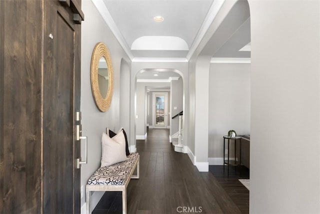 hallway featuring dark wood-type flooring, ornamental molding, arched walkways, baseboards, and stairs