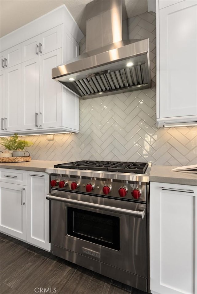 kitchen featuring luxury stove, white cabinets, light countertops, and wall chimney range hood