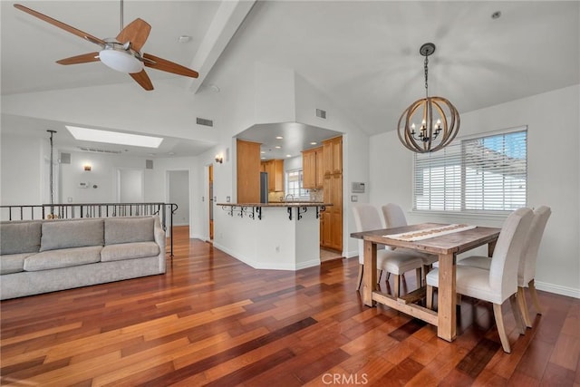 dining room with high vaulted ceiling, dark hardwood / wood-style floors, a skylight, and ceiling fan with notable chandelier