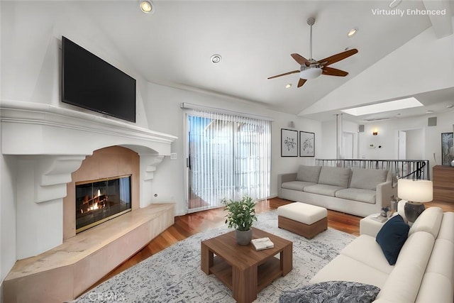 living room with vaulted ceiling, ceiling fan, a high end fireplace, and light hardwood / wood-style floors