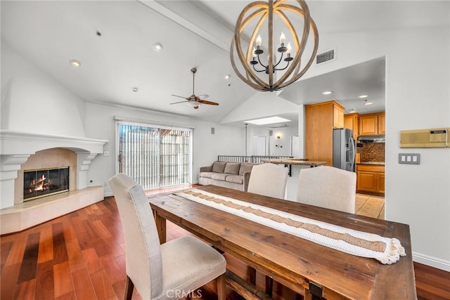 dining room with ceiling fan with notable chandelier, a fireplace, lofted ceiling with beams, and light wood-type flooring