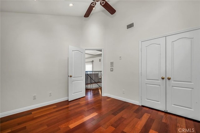 unfurnished bedroom featuring ceiling fan, a towering ceiling, dark hardwood / wood-style flooring, and a closet