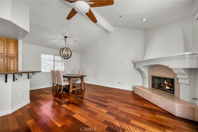 dining area with lofted ceiling with beams, ceiling fan with notable chandelier, a fireplace, and dark hardwood / wood-style flooring