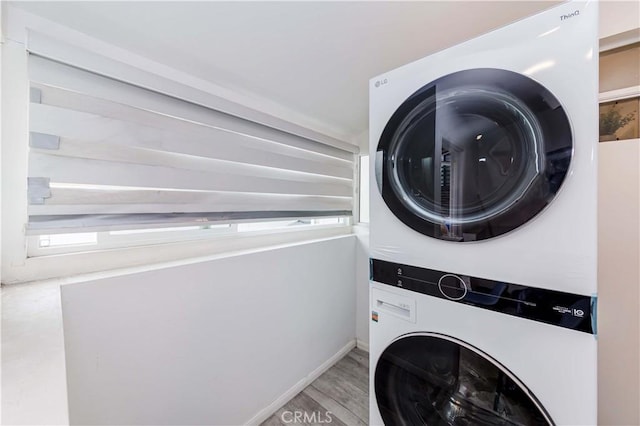 washroom featuring stacked washer and dryer, a healthy amount of sunlight, and light hardwood / wood-style flooring