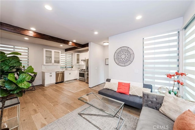 living room featuring beam ceiling, light hardwood / wood-style flooring, and a wealth of natural light