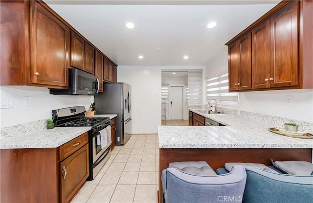 kitchen with appliances with stainless steel finishes, sink, a breakfast bar area, light stone counters, and kitchen peninsula