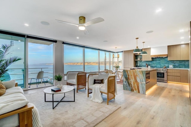 living room featuring light wood-type flooring, a wall of windows, ceiling fan, and a water view