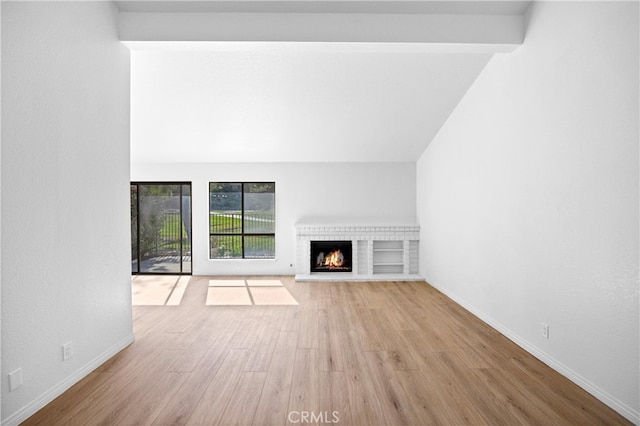 unfurnished living room featuring lofted ceiling, a fireplace, baseboards, and wood finished floors