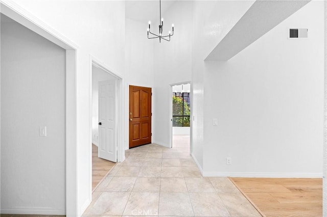 hall with light tile patterned floors, visible vents, a high ceiling, an inviting chandelier, and baseboards